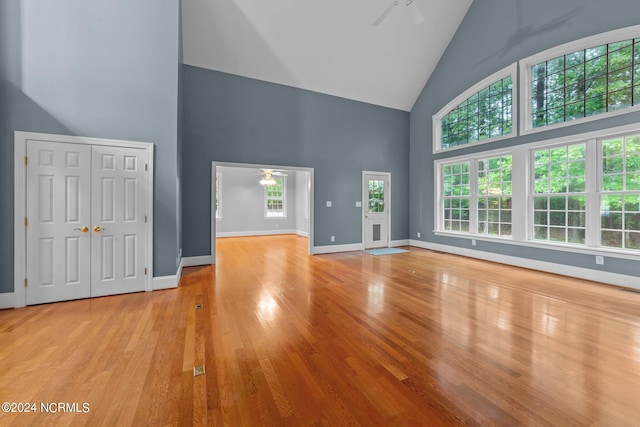 unfurnished living room with baseboards, ceiling fan, high vaulted ceiling, and wood finished floors