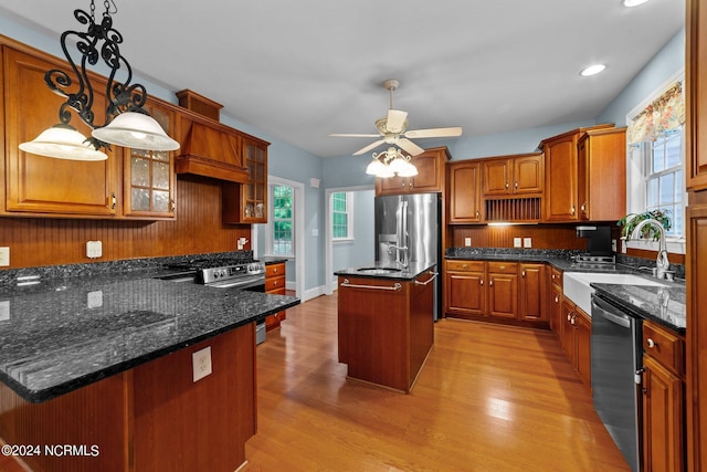 kitchen featuring a center island with sink, glass insert cabinets, appliances with stainless steel finishes, light wood-style floors, and a sink