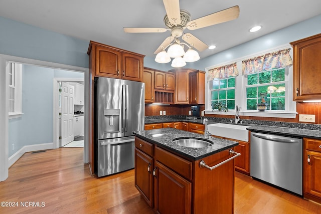 kitchen with stainless steel appliances, dark stone counters, a sink, and a center island with sink