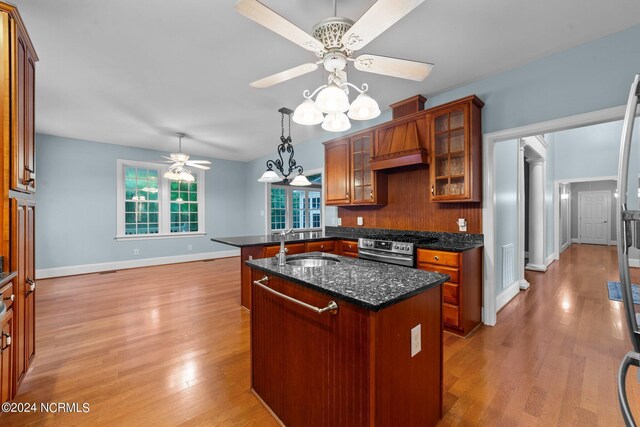 kitchen with light hardwood / wood-style flooring, ceiling fan, an island with sink, and stainless steel stove