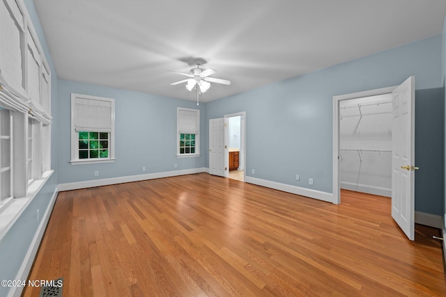 unfurnished bedroom featuring a spacious closet, a closet, light wood-style flooring, and baseboards