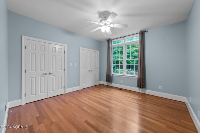 unfurnished bedroom with light wood-style flooring, baseboards, and two closets