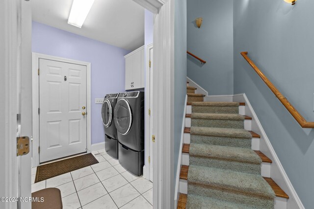 clothes washing area featuring washing machine and dryer, light tile patterned floors, and cabinets