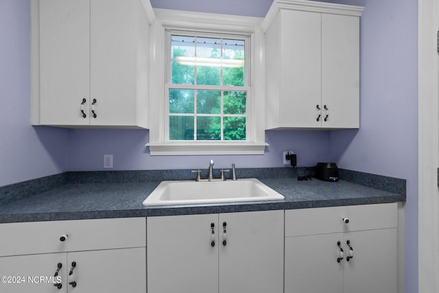 kitchen with dark countertops, white cabinets, and a sink