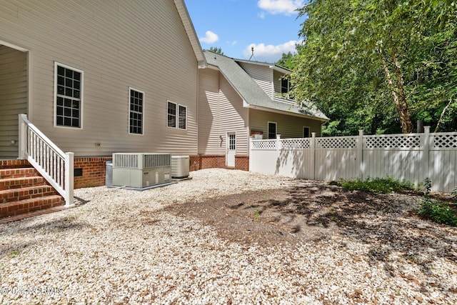 view of side of home with a shingled roof, cooling unit, and fence