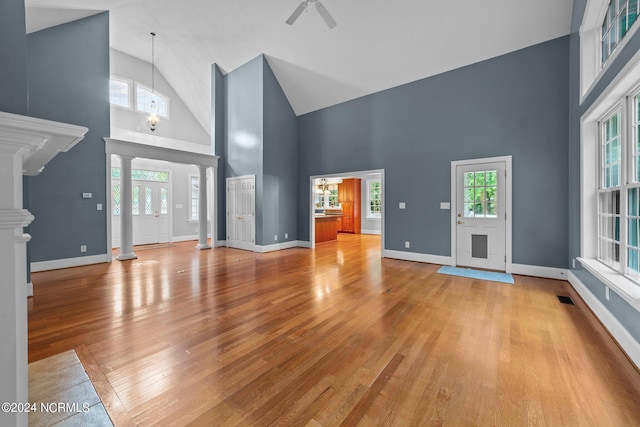 unfurnished living room with high vaulted ceiling, light hardwood / wood-style floors, a healthy amount of sunlight, and ornate columns