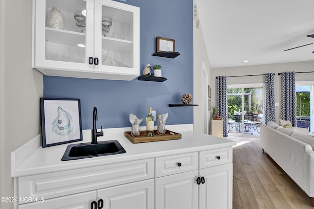 kitchen with light wood finished floors, glass insert cabinets, light countertops, white cabinetry, and a sink