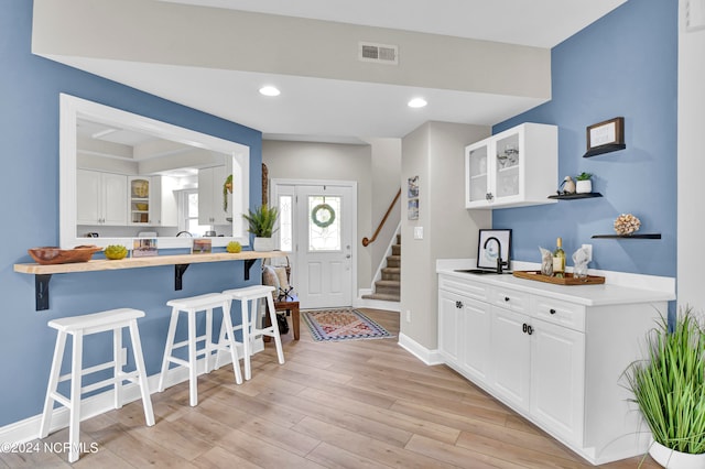 interior space with a breakfast bar area, light hardwood / wood-style flooring, white cabinetry, and sink