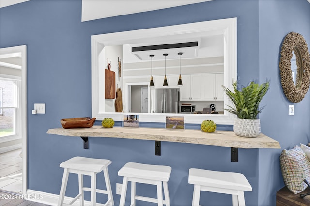 kitchen with a breakfast bar area, tile patterned floors, stainless steel appliances, light countertops, and white cabinetry