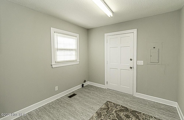 unfurnished room with a textured ceiling, light hardwood / wood-style floors, and electric panel