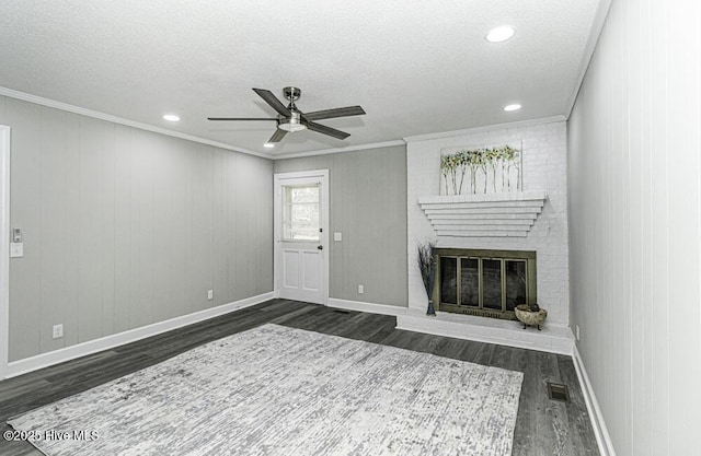 unfurnished living room featuring a brick fireplace, crown molding, dark wood-type flooring, and a textured ceiling