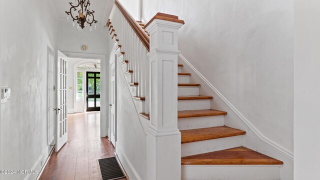 stairs featuring hardwood / wood-style floors, a chandelier, and french doors