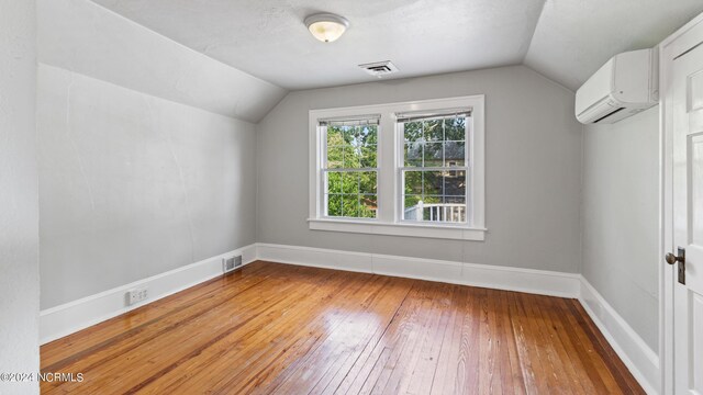 additional living space featuring lofted ceiling, an AC wall unit, and wood-type flooring