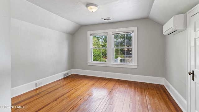 additional living space with vaulted ceiling, a wall unit AC, wood finished floors, and visible vents