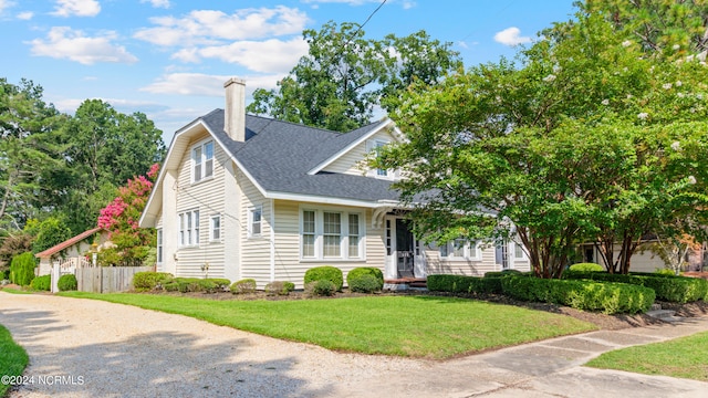 view of front of house with fence, roof with shingles, a front lawn, a chimney, and gravel driveway