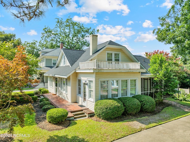 back of property featuring a balcony, a sunroom, a yard, roof with shingles, and a chimney