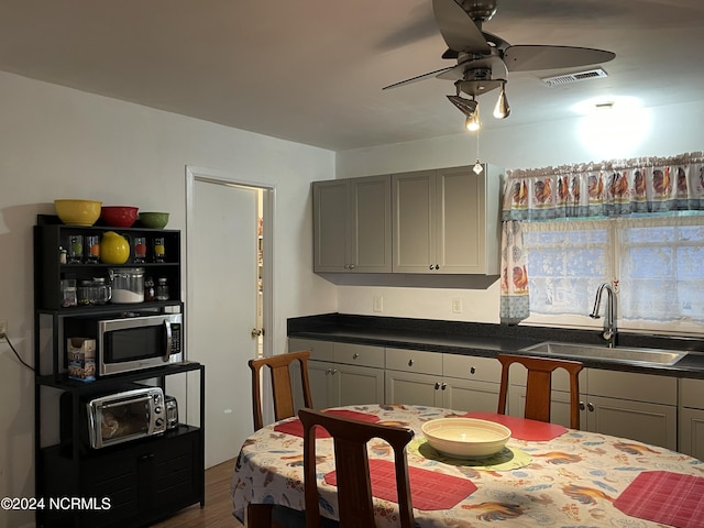 kitchen featuring stainless steel microwave, dark countertops, a sink, and gray cabinetry