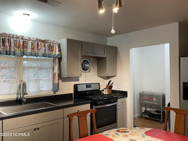 kitchen with gray cabinets, stainless steel range with gas stovetop, a sink, and visible vents