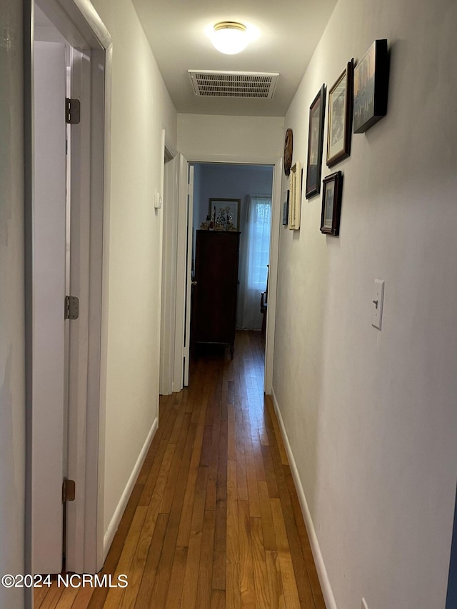 hall with baseboards, visible vents, and hardwood / wood-style floors