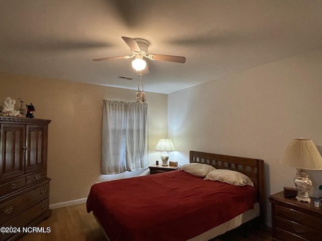 bedroom with a ceiling fan, visible vents, baseboards, and wood finished floors