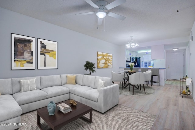 living room with a textured ceiling, light hardwood / wood-style flooring, and ceiling fan with notable chandelier