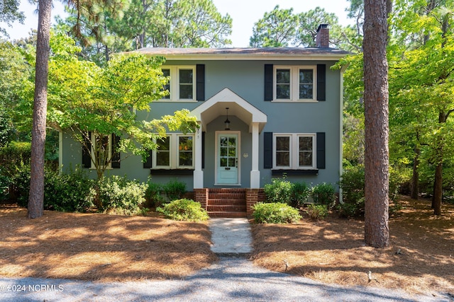 colonial-style house with entry steps, a chimney, and stucco siding