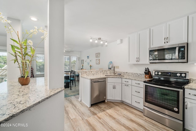 kitchen with white cabinets, stainless steel appliances, kitchen peninsula, and light stone counters