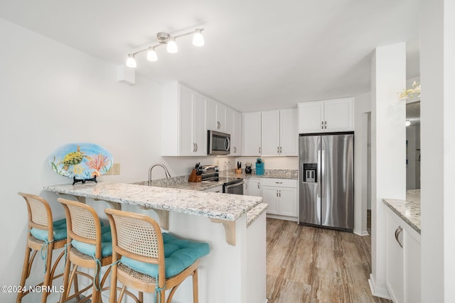 kitchen featuring white cabinets, kitchen peninsula, a breakfast bar area, and appliances with stainless steel finishes