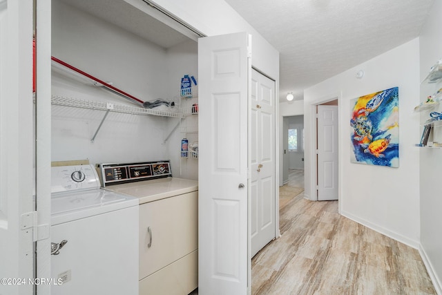 clothes washing area with light wood-type flooring, a textured ceiling, and washing machine and clothes dryer