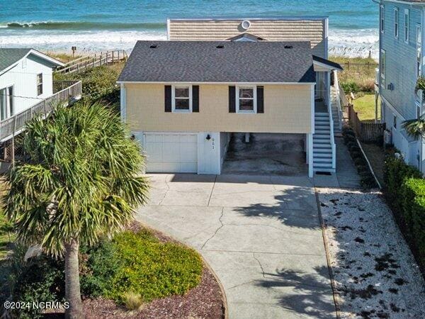 exterior space with a view of the beach, concrete driveway, a water view, stairway, and a garage