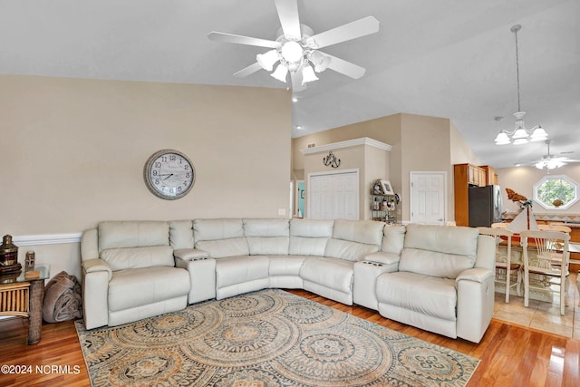 living area with lofted ceiling, light wood-style flooring, and ceiling fan with notable chandelier