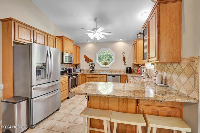 kitchen featuring appliances with stainless steel finishes, decorative backsplash, kitchen peninsula, ceiling fan, and a breakfast bar