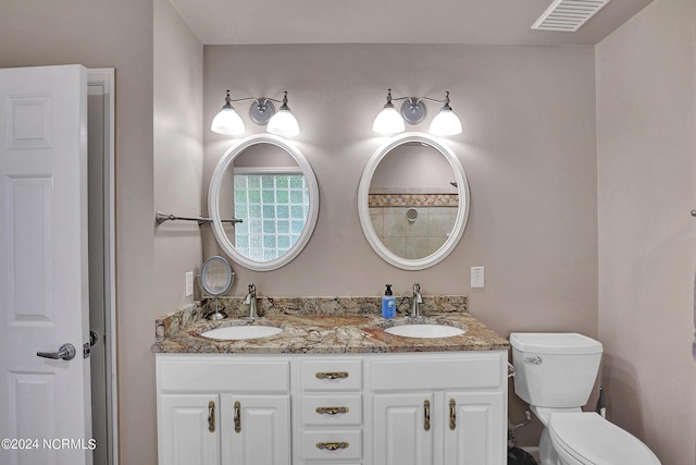 full bath with toilet, double vanity, a sink, and visible vents