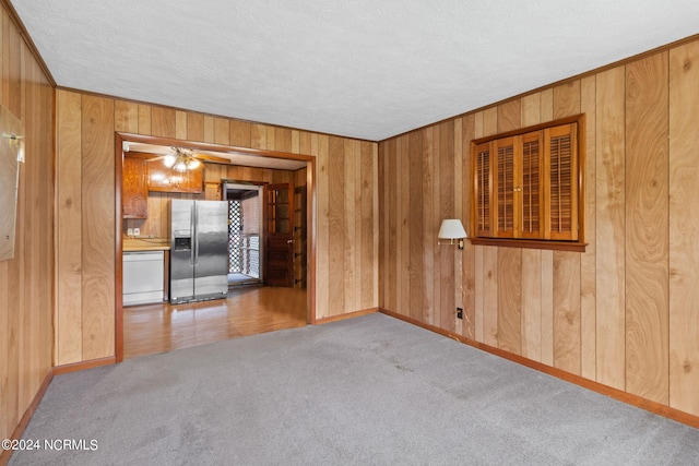 empty room featuring a textured ceiling, wooden walls, light colored carpet, and ornamental molding