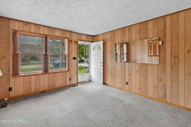 carpeted spare room featuring a textured ceiling and wood walls