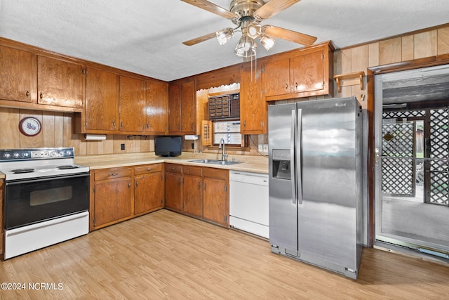 kitchen featuring white appliances, light hardwood / wood-style flooring, sink, a textured ceiling, and wooden walls