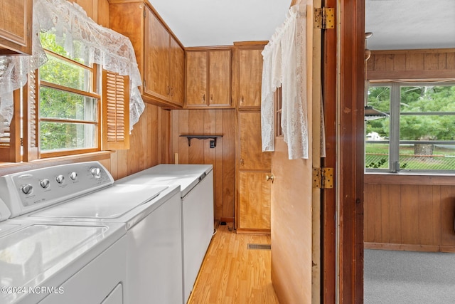 laundry room with cabinets, washer and clothes dryer, wood walls, and light wood-type flooring