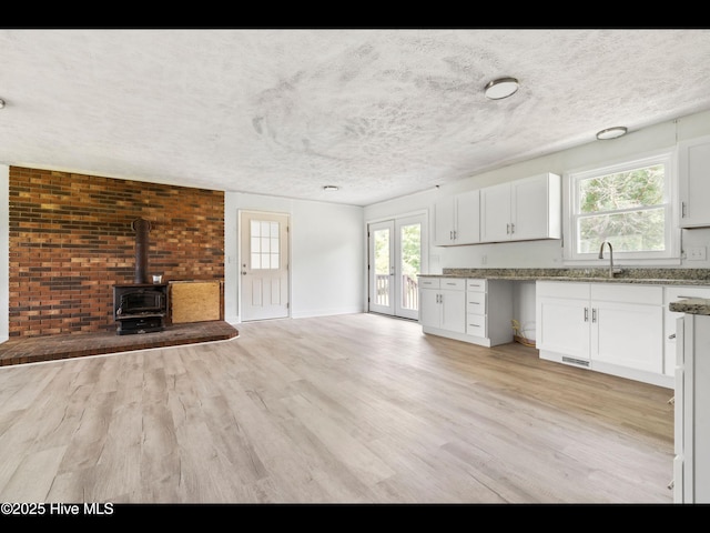 9348 NC Highway 210, Rocky Point, NC 28457 - unfurnished living room featuring a wood stove, light wood-style flooring, a sink, healthy amount of natural light, and a textured ceiling