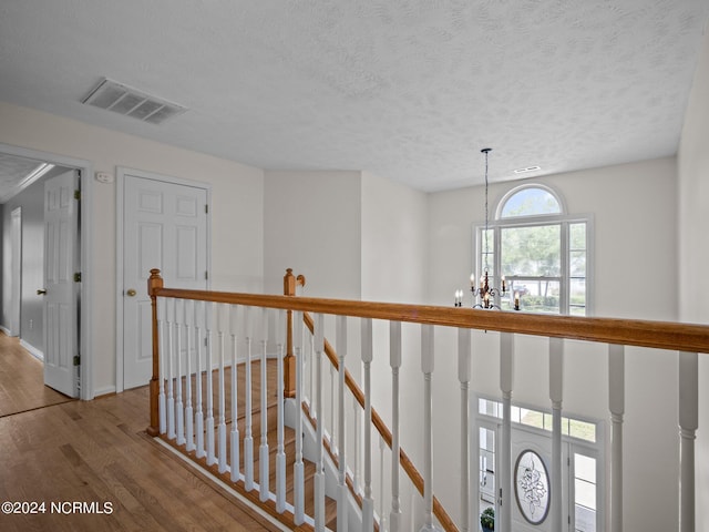 corridor with an inviting chandelier, a textured ceiling, and hardwood / wood-style flooring