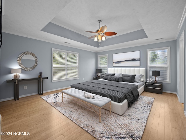 bedroom featuring ornamental molding, a tray ceiling, light hardwood / wood-style floors, and ceiling fan