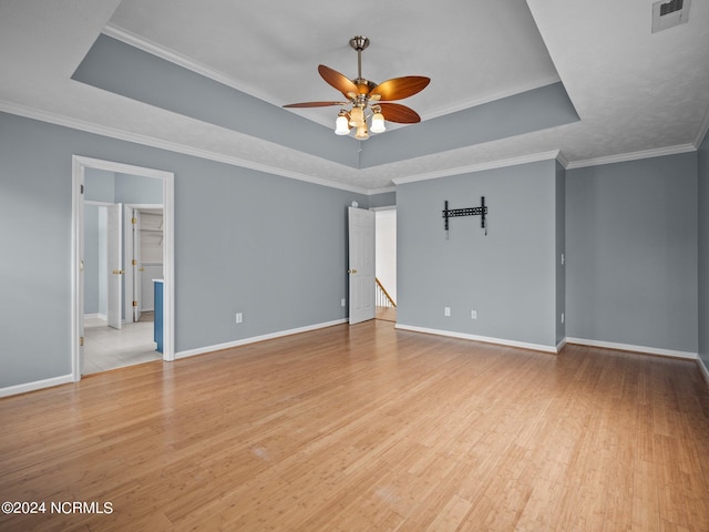 unfurnished bedroom featuring ceiling fan, a raised ceiling, ornamental molding, light hardwood / wood-style flooring, and ensuite bath