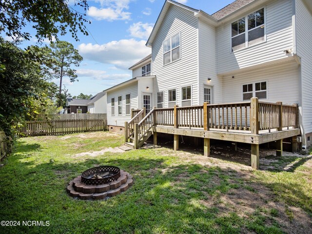 rear view of property featuring a yard, a wooden deck, and a fire pit