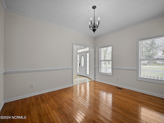 unfurnished room with crown molding, light hardwood / wood-style floors, an inviting chandelier, and a wealth of natural light