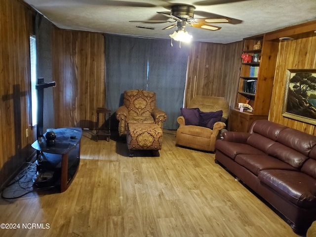 living room with ceiling fan, built in features, light hardwood / wood-style floors, and wood walls