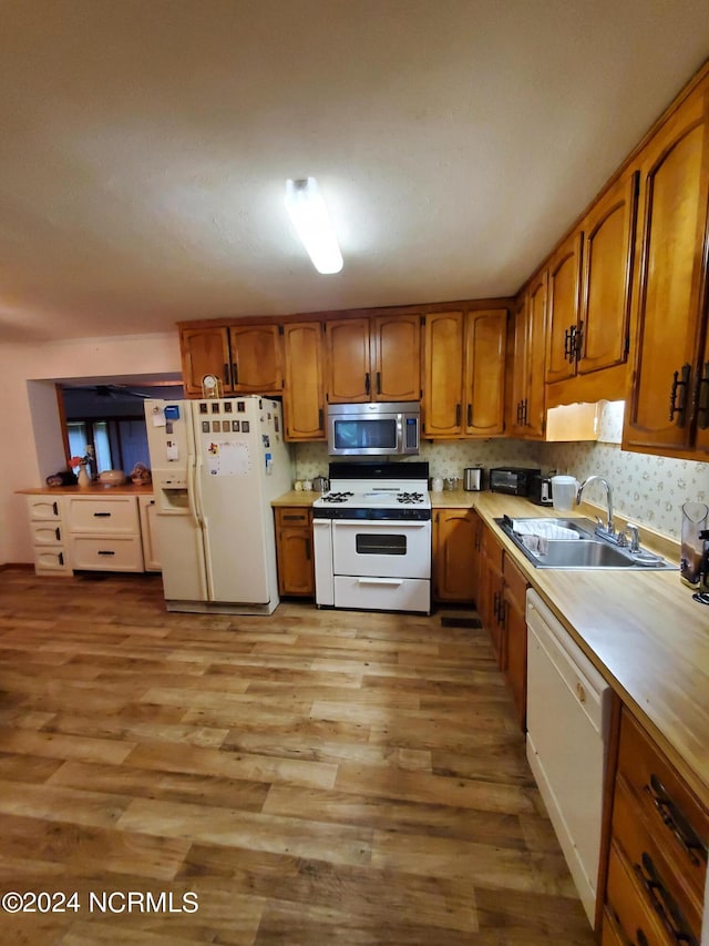 kitchen with light wood-type flooring, white appliances, backsplash, and sink