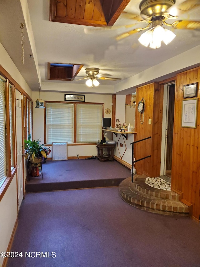 interior space featuring ceiling fan, dark carpet, and wooden walls