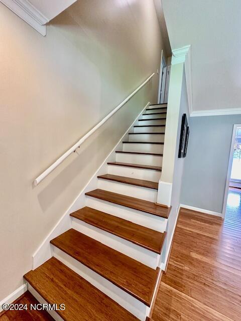 stairway with wood-type flooring and ornamental molding