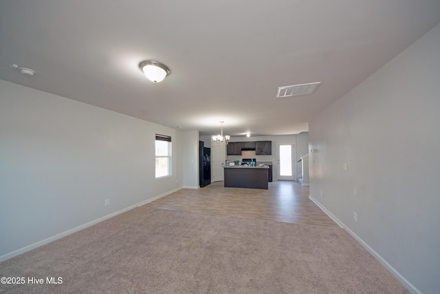 unfurnished living room featuring light carpet, a healthy amount of sunlight, and a notable chandelier