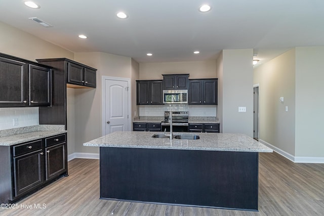 kitchen featuring a kitchen island with sink, stainless steel appliances, light stone countertops, sink, and hardwood / wood-style floors