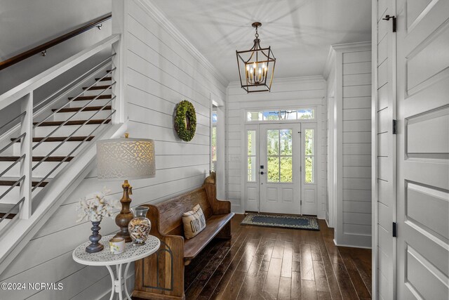 foyer entrance with crown molding, dark wood-type flooring, a chandelier, and wood walls